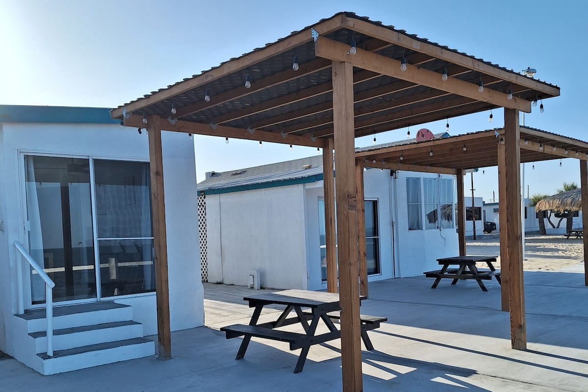 Une pergola en bois agrémentée de guirlandes lumineuses, une table de pique-nique et un espace salon abrité.
