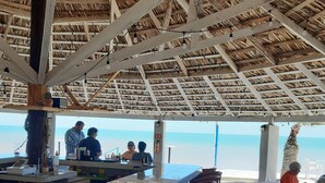 Een strandbar met rieten dak, houten stoelen en uitzicht op de oceaan.