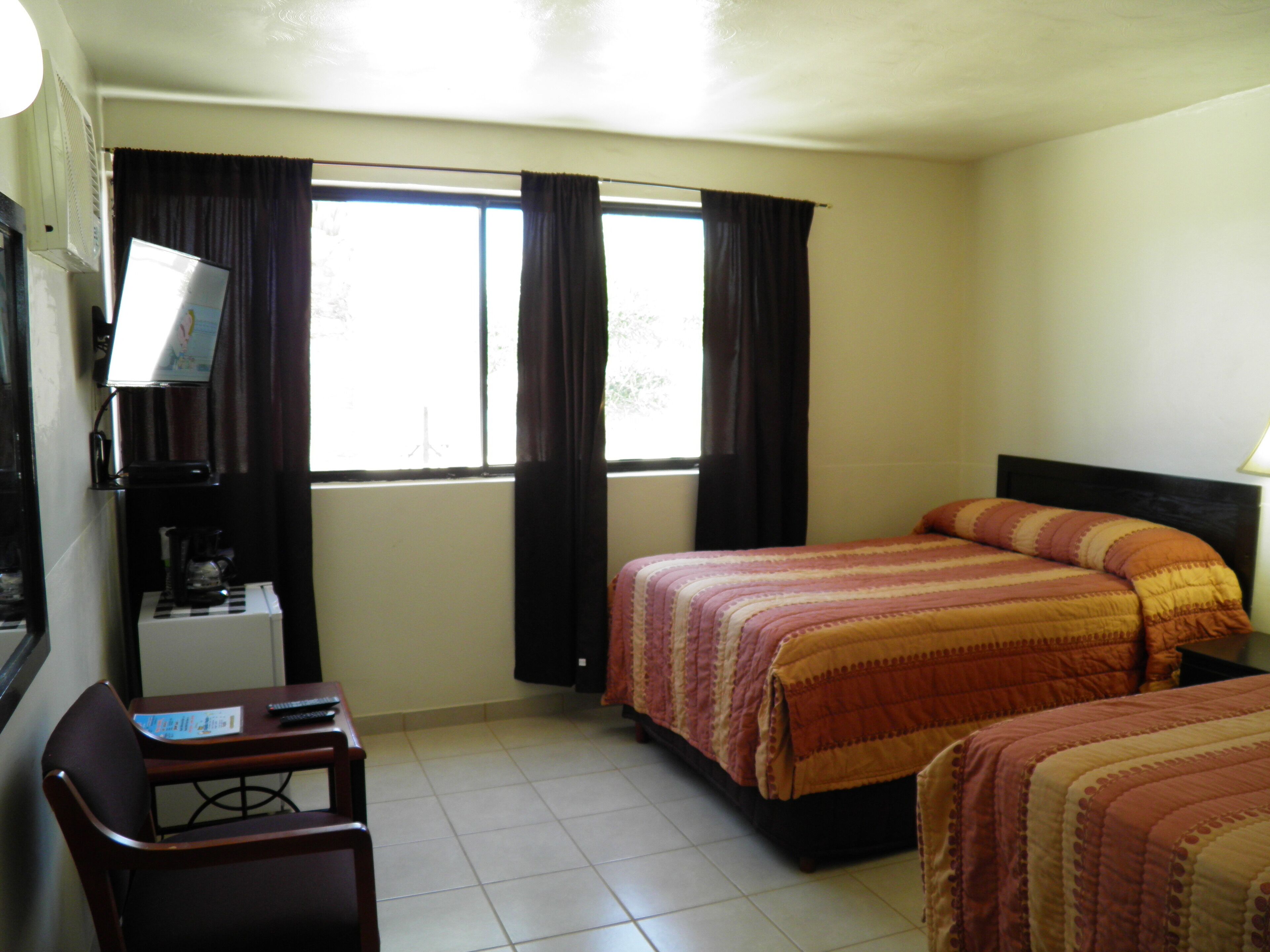 Habitación de hotel con dos camas, un escritorio con silla, cafetera y ventana con cortinas.