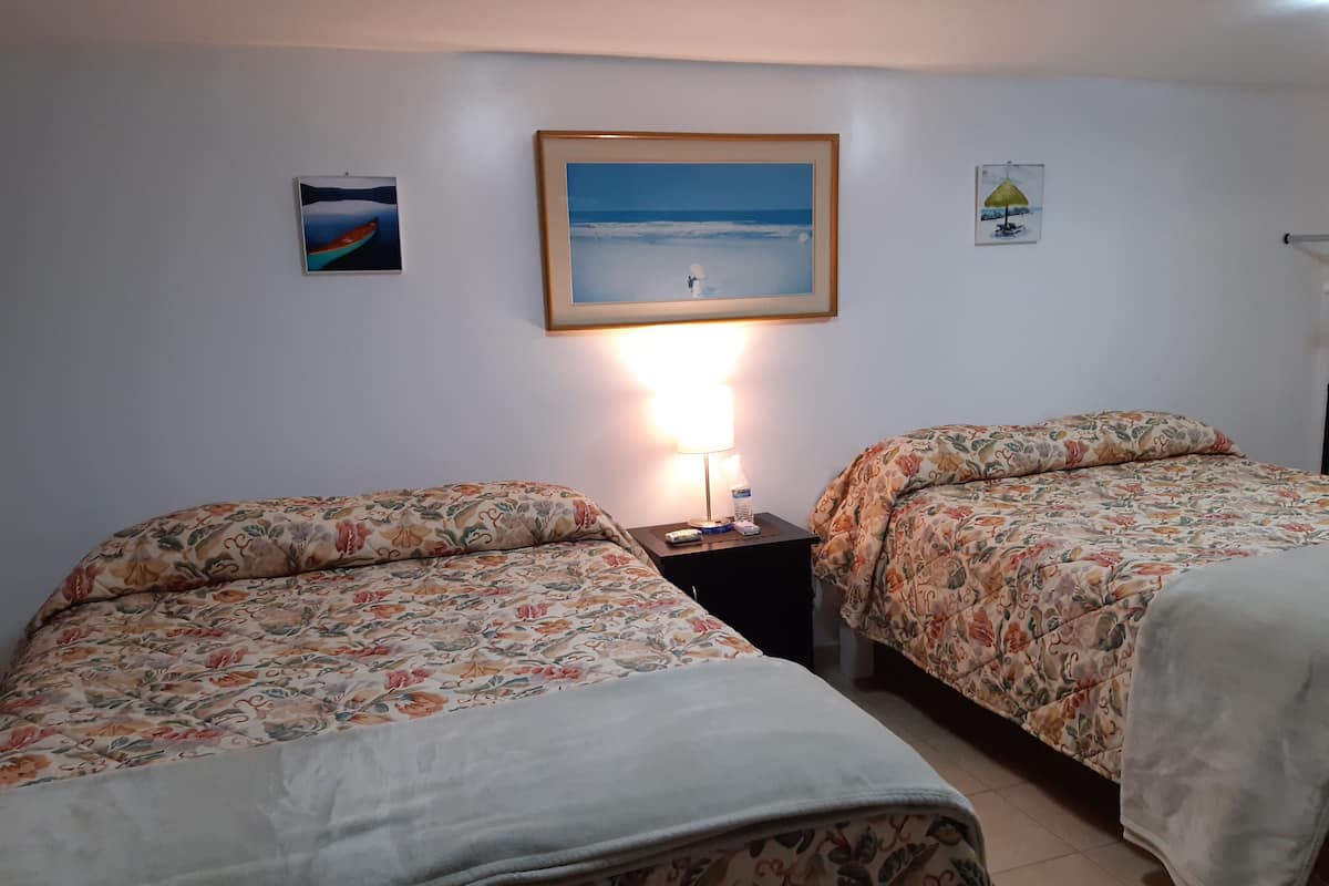 Une chambre avec deux lits, chacun agrémenté de draps à motifs floraux, une table de chevet avec une lampe et des tableaux encadrés accrochés au mur.