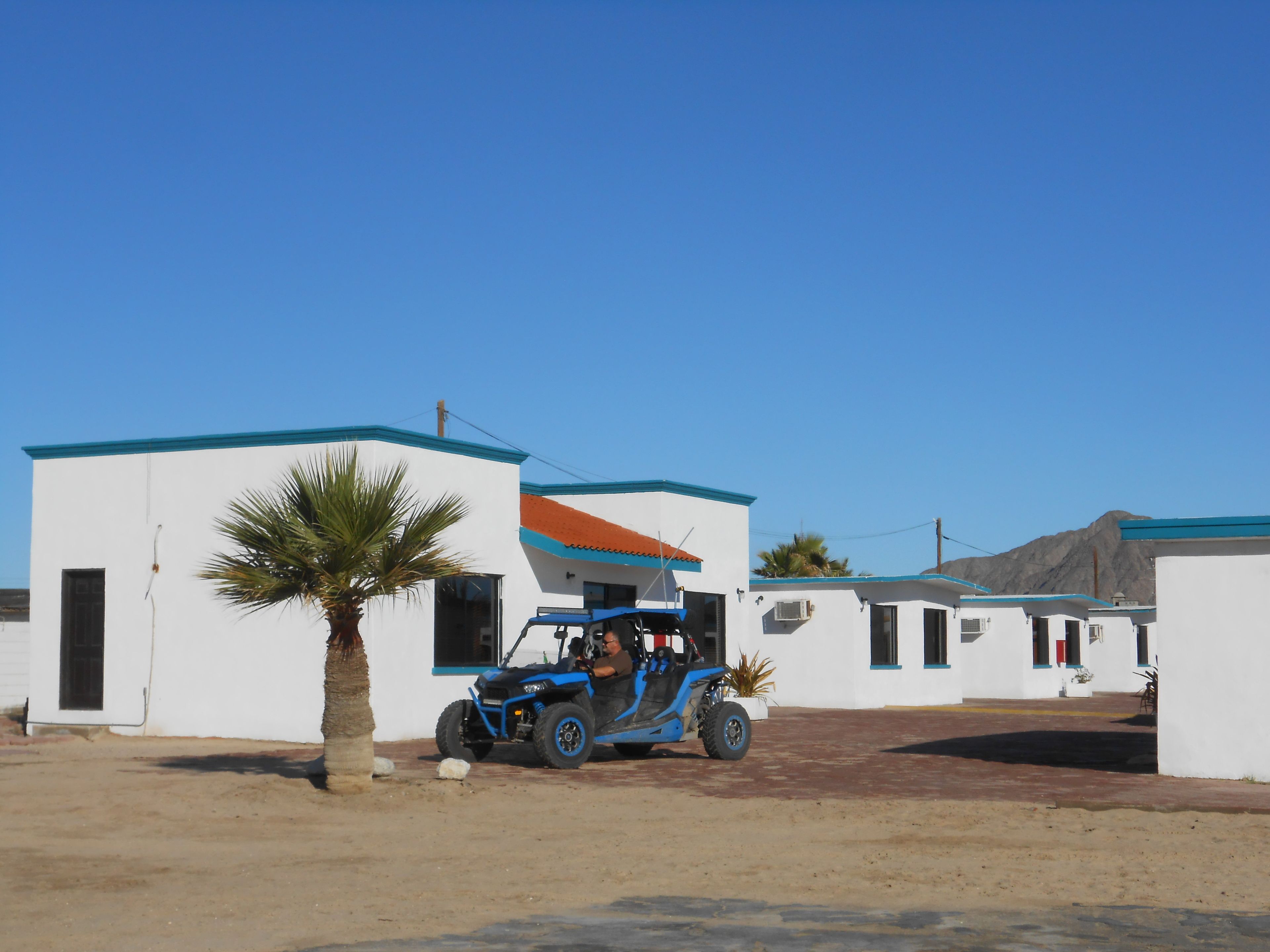 A building with a white exterior and blue trim, a blue vehicle parked in front, and a palm tree nearby.