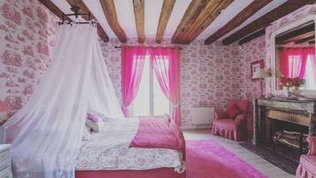 A bedroom with a canopy bed, pink curtains, a fireplace, and patterned wallpaper.