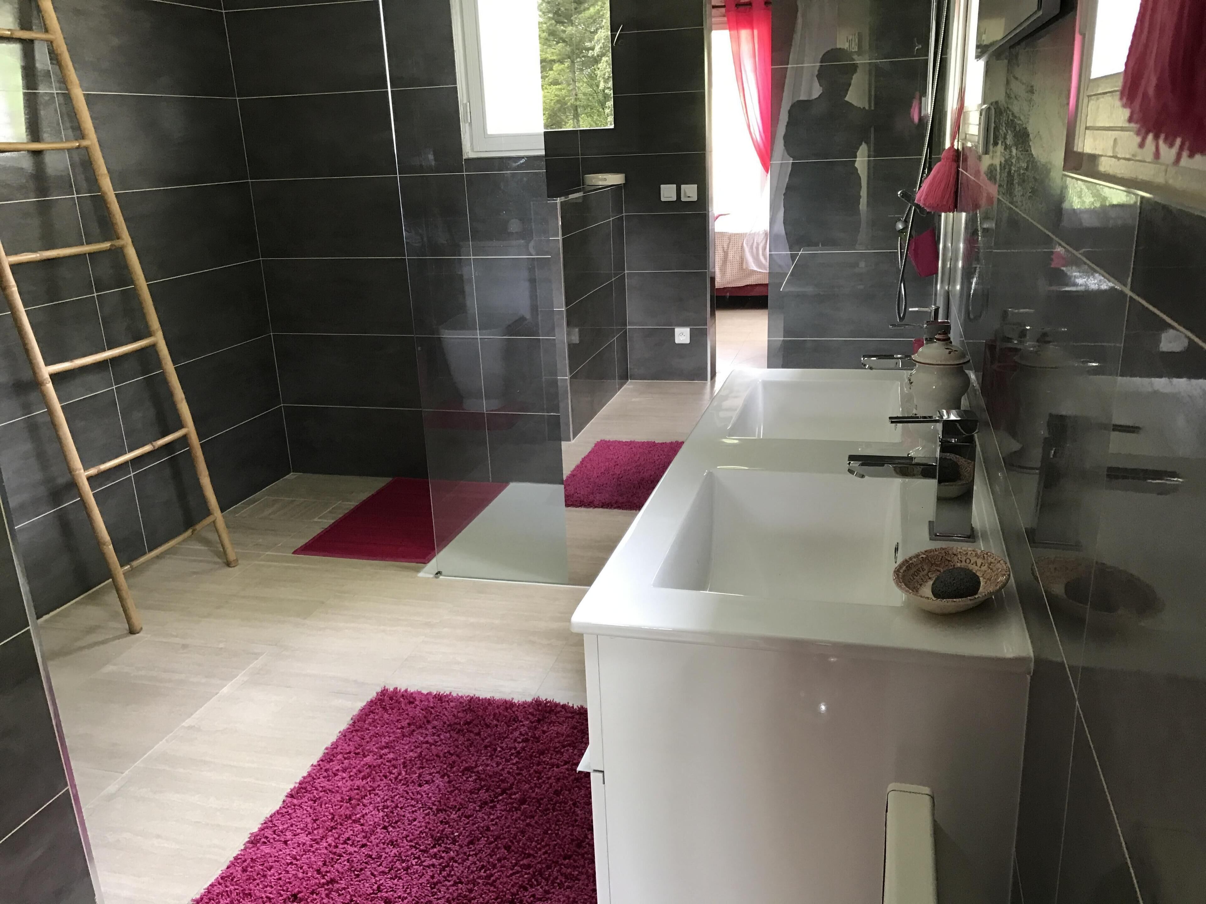 A modern bathroom with black tiles, a white bathtub, a mirror, and a red rug.