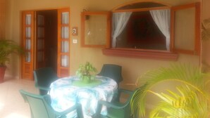 Um quarto com uma mesa, cadeiras, uma janela com cortinas e um ventilador de teto.