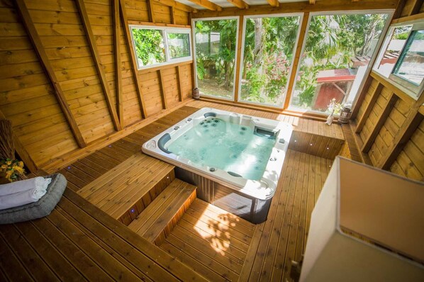 A wooden deck with a hot tub, large windows, and a view of greenery. - Locastudio "Grenadine", Countryside and beach - T3 (Sainte-Anne)