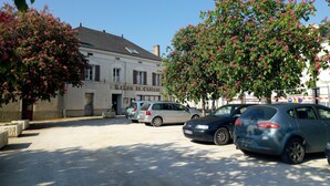 A parking lot with several cars, a building labeled "Relais du Chateau", and trees with pink flowers. - Le Relais du Château (Plaine-et-Vallées)