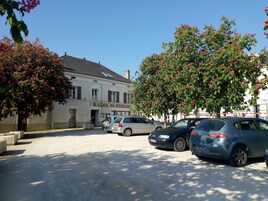 Un estacionamiento con varios autos, un edificio con la leyenda "Relais du Chateau" y árboles con flores rosadas.