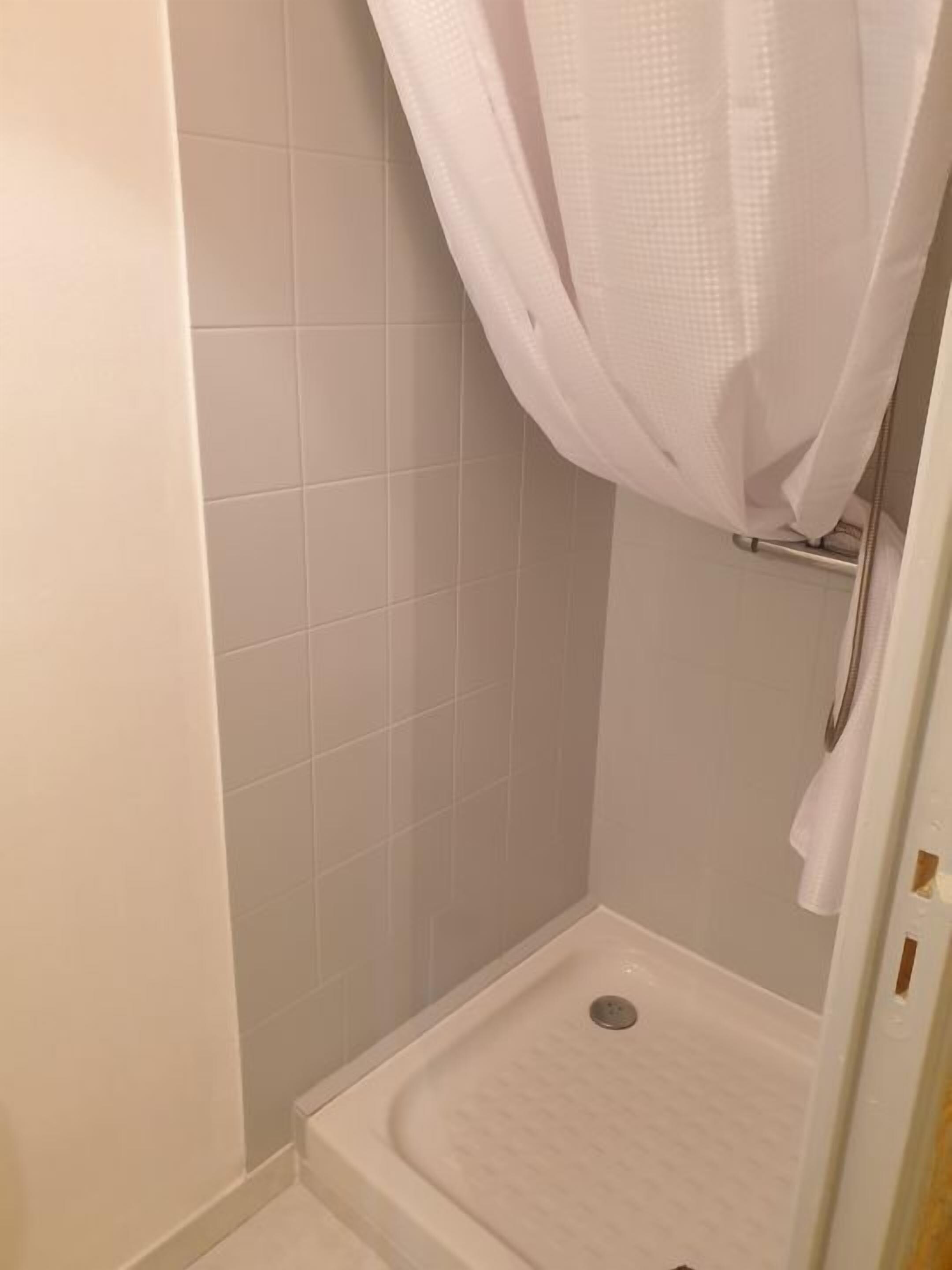 A small, white-tiled shower stall with a shower curtain.