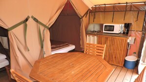Uma tenda com mesa e cadeiras de madeira, uma cama e uma kitchenette com micro-ondas.