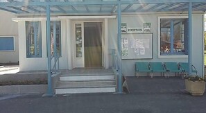 A building with a reception area, marked by a sign, and a set of green chairs outside. - Camping d'Audinet - Résidence Toilée (Brives-Charensac)