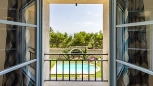 An open balcony with a view of a swimming pool, surrounded by greenery and a stone wall. - Beautiful stone property with view and heated pool, 6 km from Gordes (Murs)