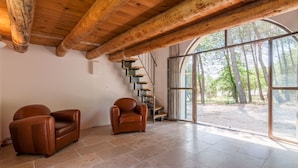 A spacious room with a high ceiling and exposed wooden beams, a large window offering a view of trees, and two leather armchairs. - Beautiful stone property with view and heated pool, 6 km from Gordes (Murs)