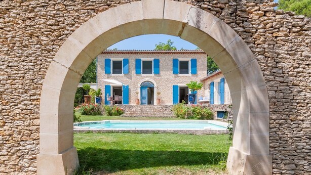 A stone archway framing a building with a pool and a well-kept lawn. - Beautiful stone property with view and heated pool, 6 km from Gordes (Murs)