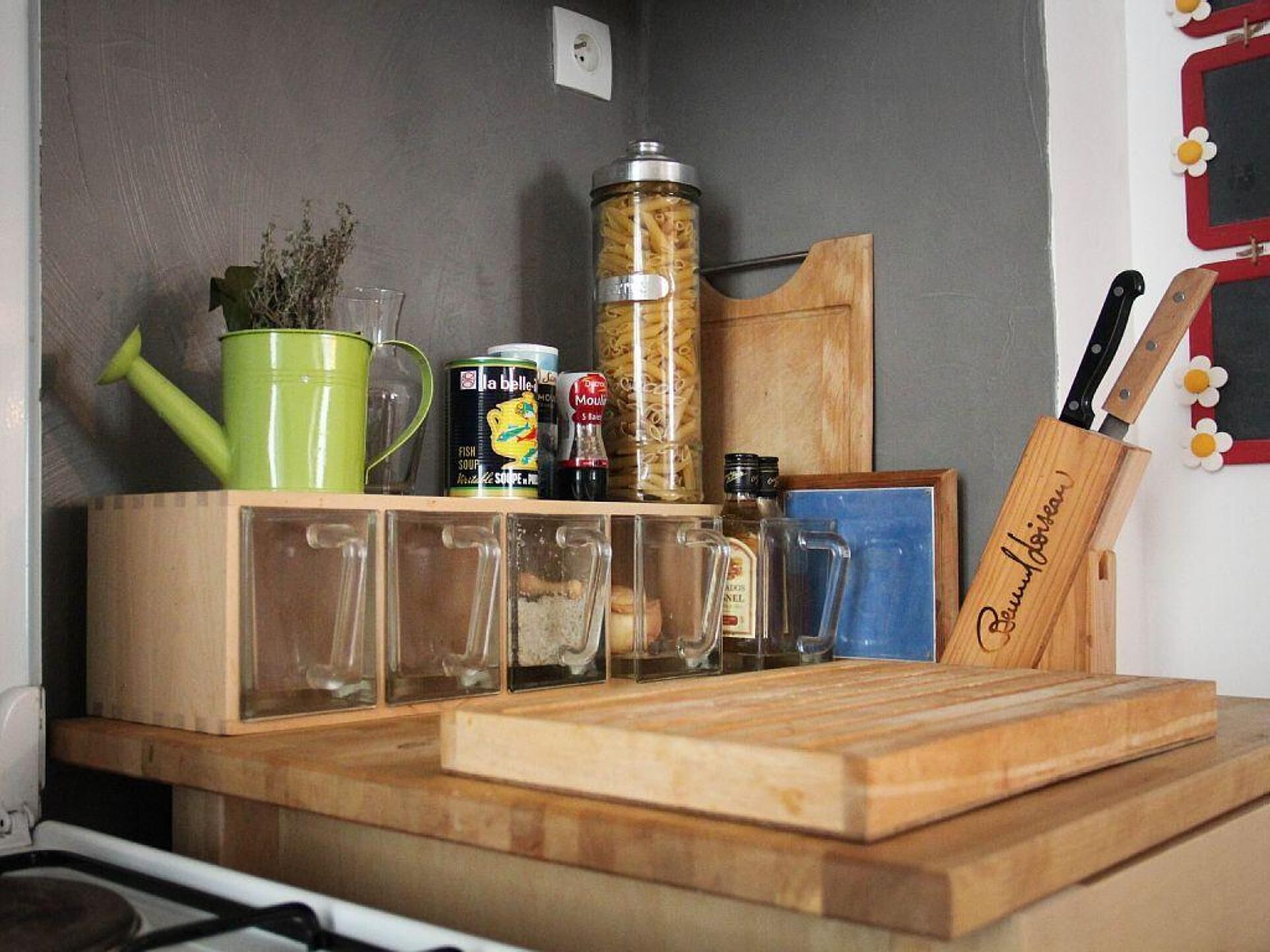 A kitchen counter with various items including a green watering can, a can of fish soup, a bottle of mustard, and a wooden cutting board.