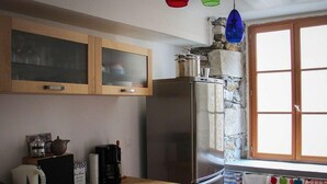 A kitchen with wooden cabinets, a stainless steel refrigerator, a window with a curtain, and a countertop with a kettle and a coffee maker.
