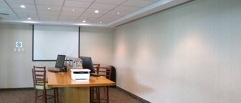 A conference room with a large table, chairs, a projector screen, and a whiteboard.
