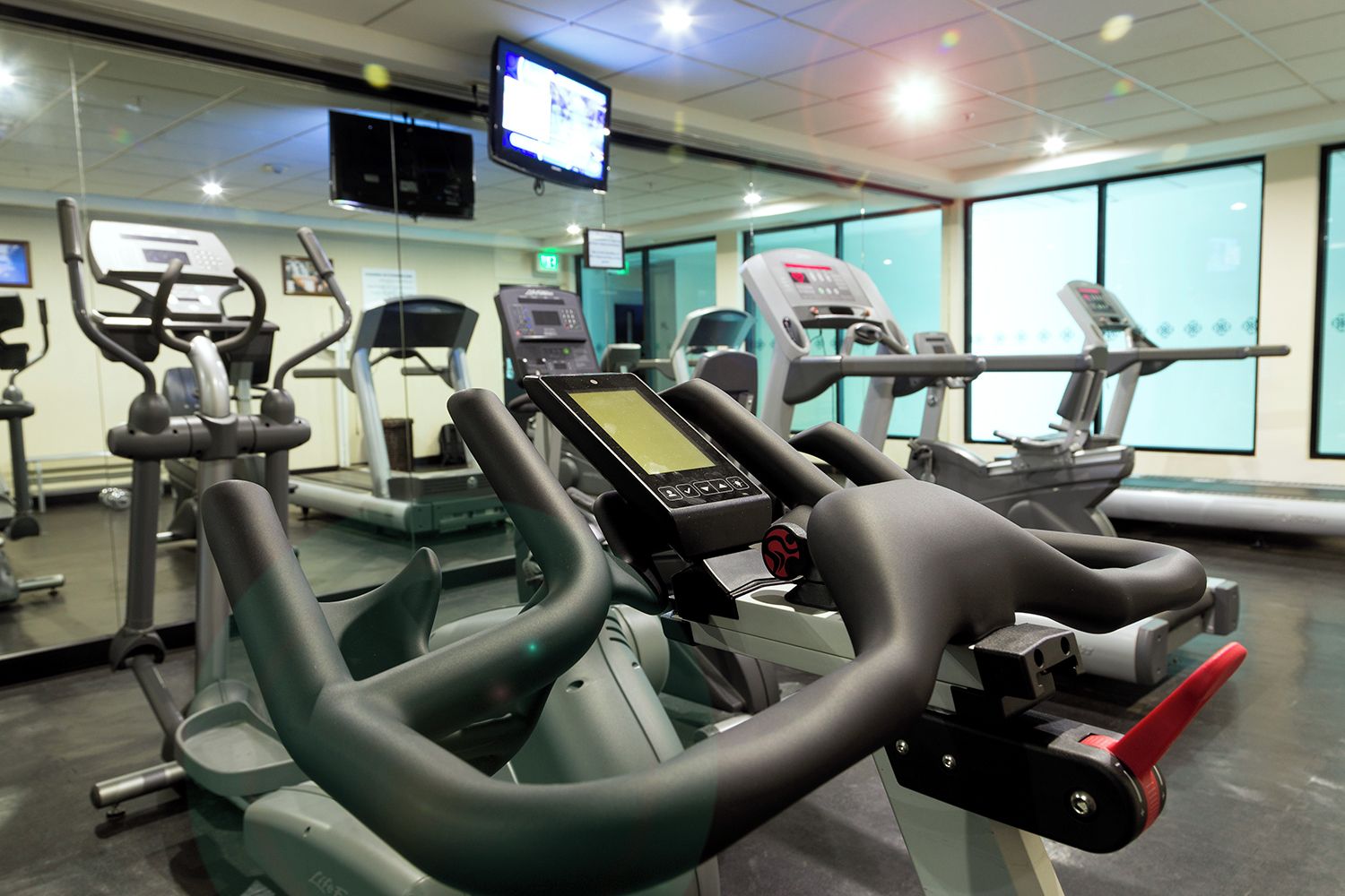 A gym with various exercise machines, including treadmills and elliptical trainers, and a digital display screen.