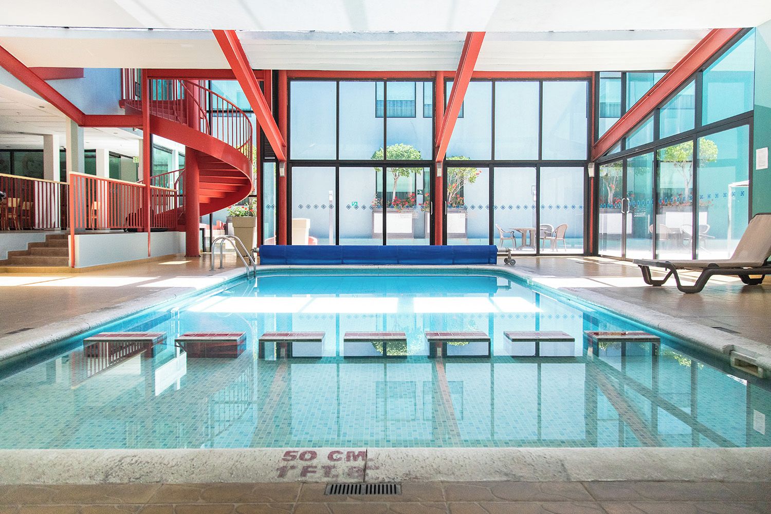 An indoor swimming pool with a blue deck, clear water, and a red staircase.