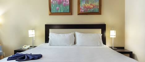 A hotel room with a large bed, two bedside lamps, a telephone, and two framed paintings on the wall.