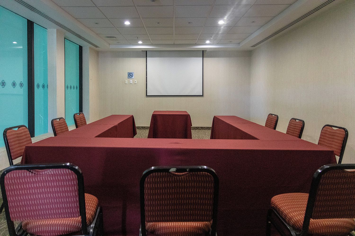 Una sala conferenze con un lungo tavolo, sedie, uno schermo per proiettore e un cartello che indica il divieto di fumare.