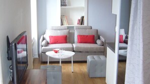 Un salon moderne avec un canapé gris, des coussins rouges, une table basse blanche et une bibliothèque.
