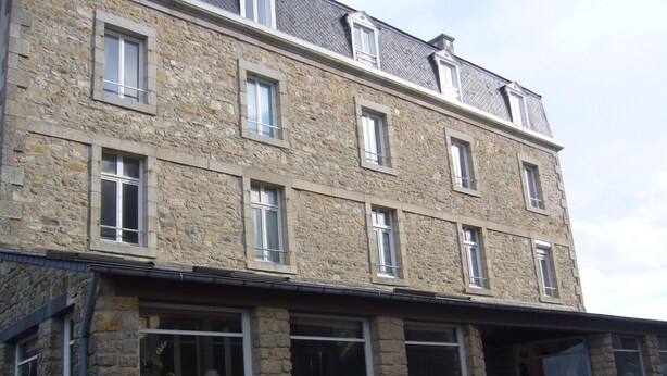 Un bâtiment en pierre à plusieurs étages, doté de nombreuses fenêtres et d’un escalier apparent menant à un niveau supérieur.