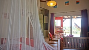 Una habitación con una cama cubierta por una mosquitera, un banco de madera y una mesa con sillas.