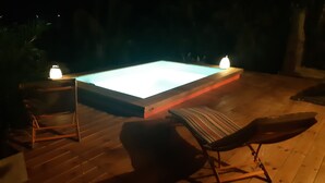 Una terraza de madera con una piscina rectangular, dos sillas reclinables y dos velas.