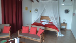 Un dormitorio con cama con dosel, un sofá, una mesa con una raqueta y pelotas de tenis, y una mesita de noche con una lámpara.