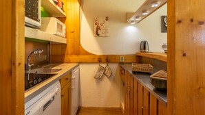 A compact kitchen with wooden cabinets, a white dishwasher, a microwave, and a hanging kitchen towel. - Apartment 4/5 PERS ARCS 1800 - WIFI (Arc 1800)