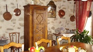 A dining area with a wooden table, chairs, a fruit bowl, and a vintage butcher sign on the wall. - Country house 4pers (Montboudif)