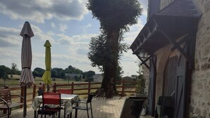 An outdoor patio area with tables and chairs, umbrellas, and a large tree. - Country house 4pers (Montboudif)