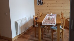 Un coin repas avec une table en bois, des chaises, un téléviseur fixé au mur et un radiateur.
