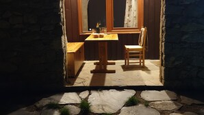 Une pièce chaleureuse et faiblement éclairée, avec un mur en pierre, une table en bois entourée de chaises et une fenêtre ornée de rideaux.