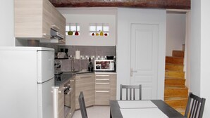 Una cuina compacta amb electrodomèstics moderns, una zona de menjador amb taula i cadires, i una escala que condueix a un altre nivell.