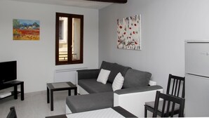 Un saló modern amb un sofà gris, una taula petita, un televisor i un frigorífic.