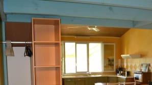 A room with a kitchen area, a dining table with chairs, and a wooden shelf unit.