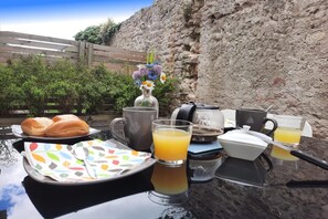Colazione servita con pane, un vaso di fiori, una tazza, un bicchiere di succo d'arancia e una moka su un tavolo.
