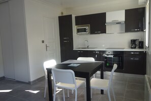 A modern kitchen with dark cabinets, a microwave, a coffee maker, and a dining table with white chairs.