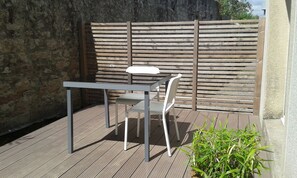 An outdoor patio with a metal table and chair, a wooden fence, and a potted plant.