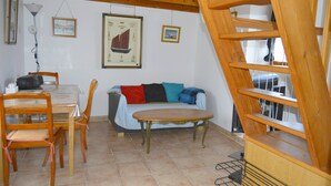 Un salon avec un escalier en bois, une table à manger avec des chaises, un canapé avec des coussins et des tableaux encadrés accrochés au mur.