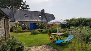 Une maison en pierre avec un toit en pente, un chemin de pierre, une table avec des chaises et un parasol bleu.