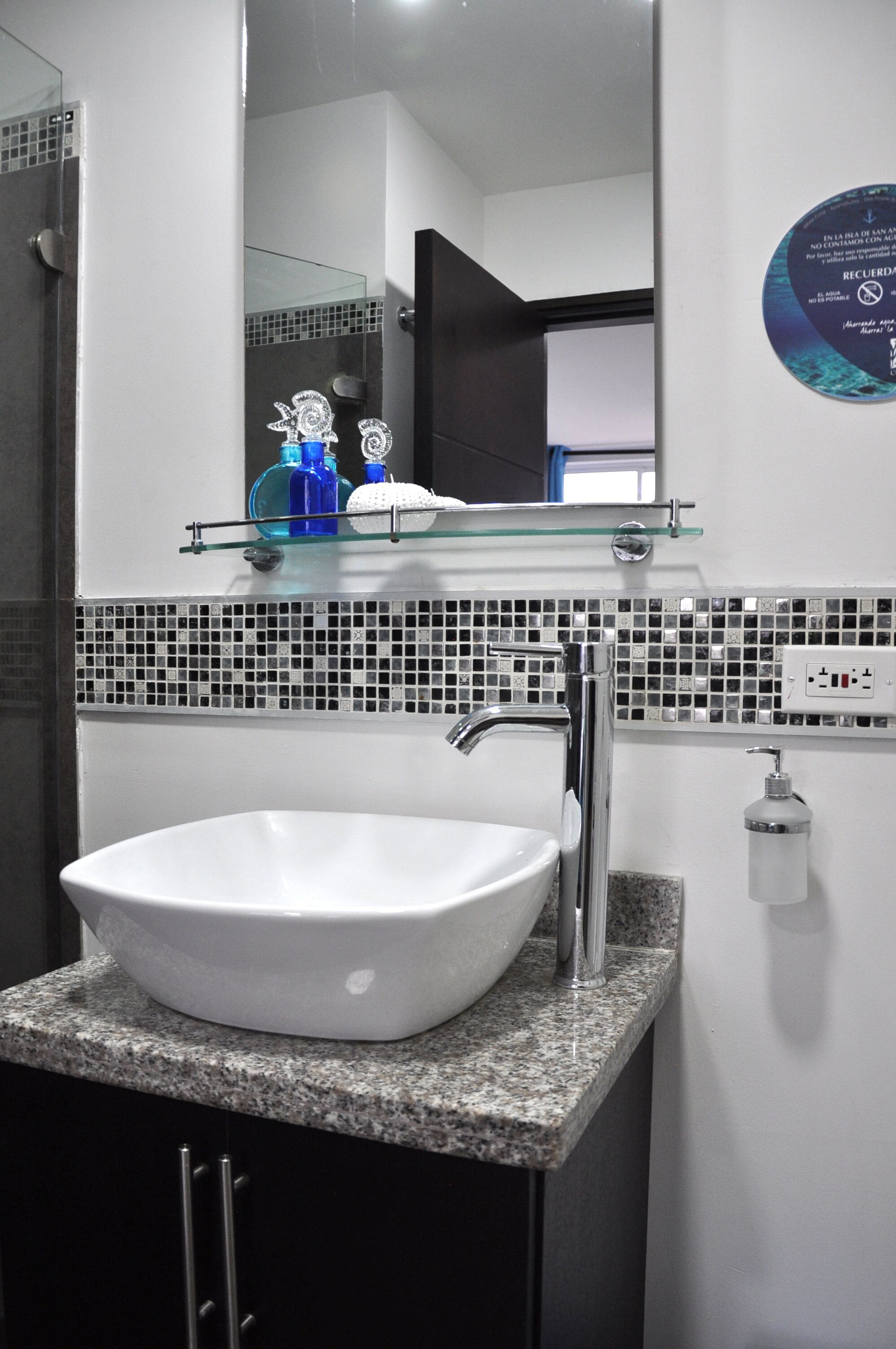 A bathroom with a white sink, a glass shelf with toiletries, and a tiled backsplash.