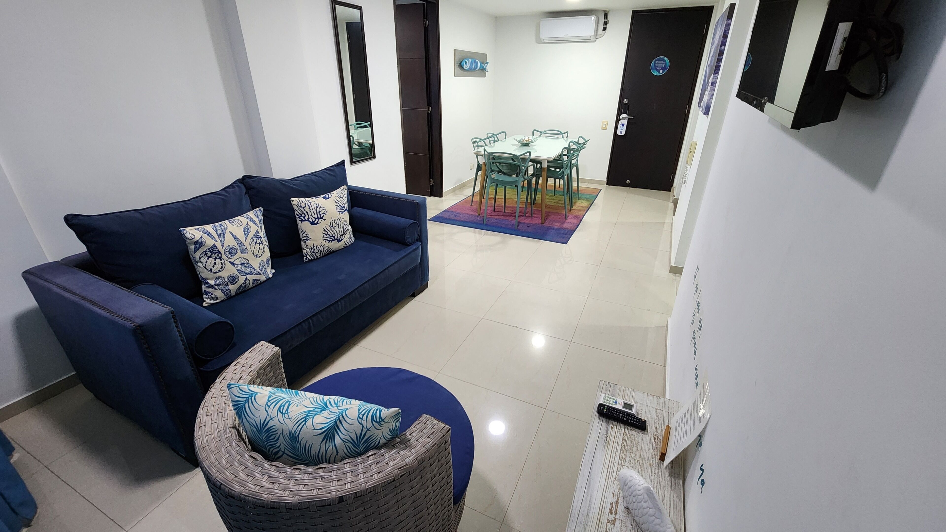 A modern living room with a blue sofa, a wicker chair, and a dining area with a table and chairs.