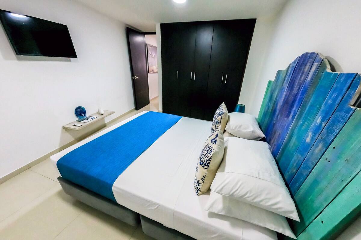 Habitación de hotel con una cama, televisor montado en la pared, armario y mesita de noche.