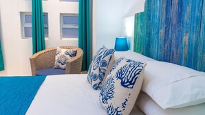 Un lit avec des oreillers à motifs blancs et bleus, une lampe bleue et une chaise en osier avec un coussin.