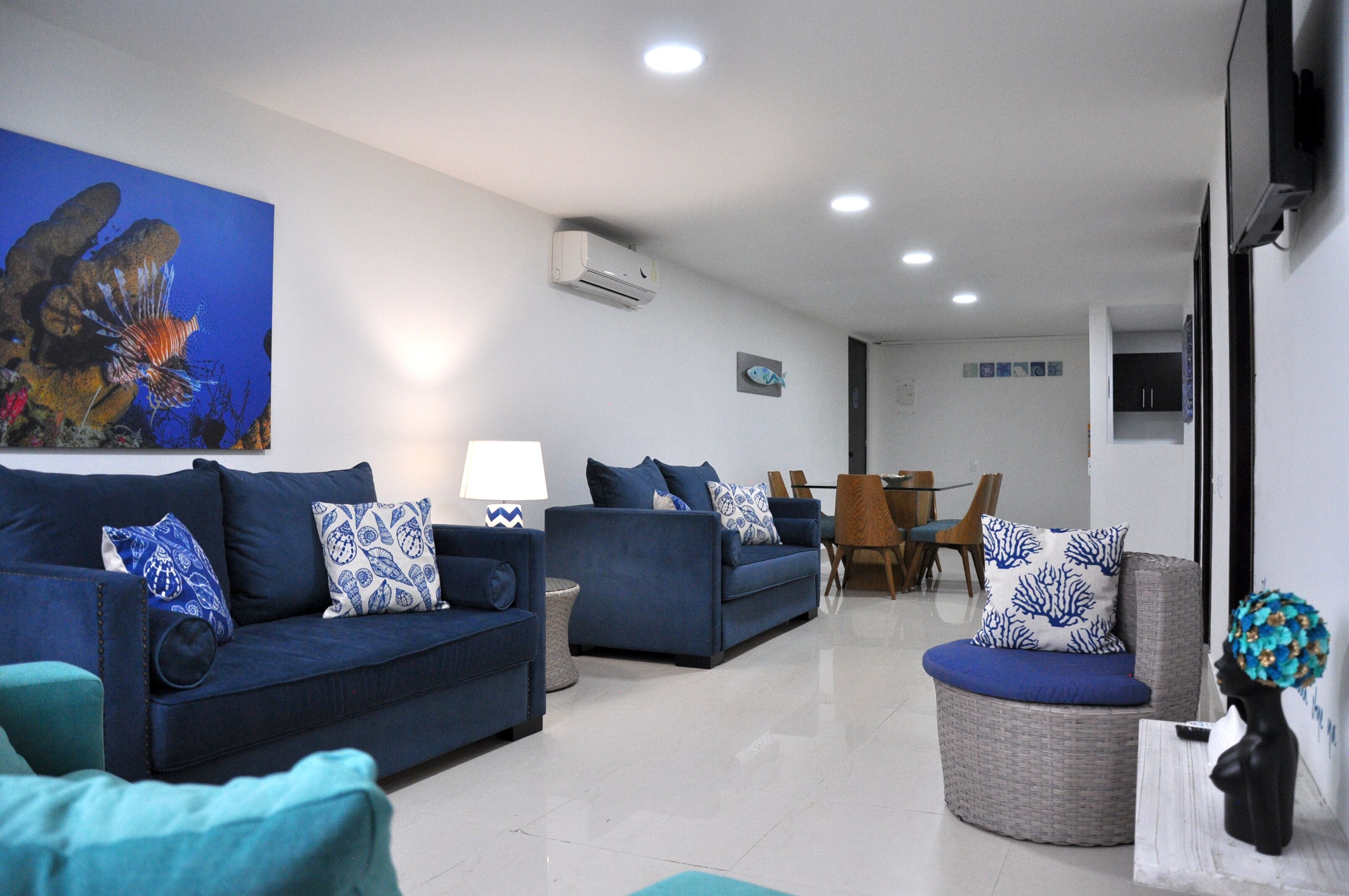 Uma sala de estar moderna com um sofá azul, uma poltrona de vime redonda e uma área de jantar com mesa e cadeiras de madeira.