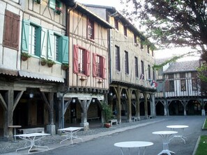 A traditional European street with timber-framed buildings, outdoor seating, and a cobblestone path.