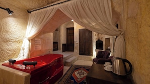 A room with a red bathtub, a coffee table with cups and a kettle, and a patterned rug. - Tafana Cave & Stone Lodge (Ürgüp)