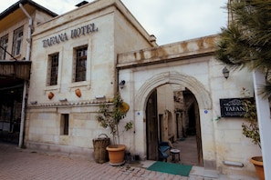 Un bâtiment portant l’inscription « HÔTEL TAFANA », avec une entrée en forme d’arc, un petit espace extérieur aménagé avec des sièges et un pot de fleurs.